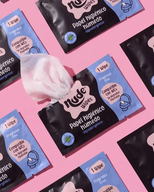 Sachets individuales de NUDE repartidos sobre fondo rosado; de uno asoma el paño.